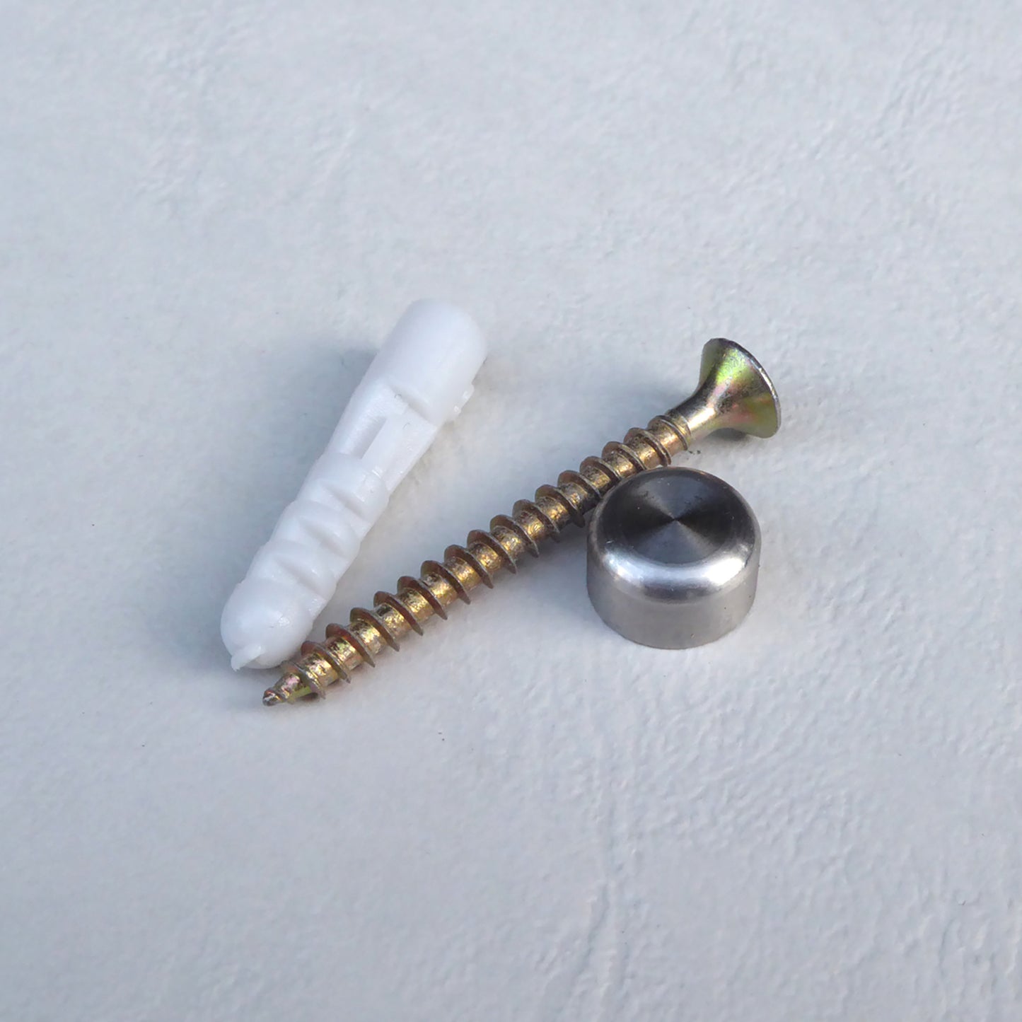 Auf einer weißen Fläche sind eine Schraube, Dübel und ein Schraubverblender abgebildet.