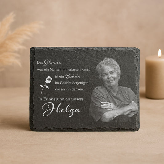 Gedenktafel mit Text 'Das Schönste, was ein Mensch hinterlassen kann, ist ein Lächeln im Gesicht derjenigen, die an ihn denken. In Erinnerung an unsere Helga' und einer weißen Rosenzeichnung.